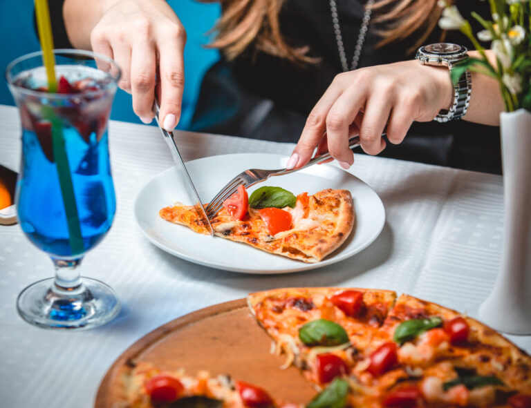 Pizzascheibe mit Tischbesteck und einem Glas des blauen Lagunencocktails